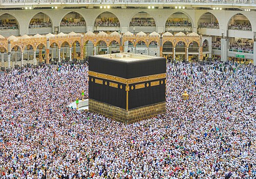 Thousands of Muslim pilgrims in white ihram clothes walking around the black cube of the Kaaba